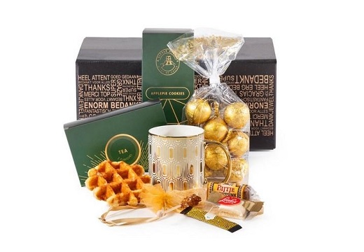 Luxe kerstpakket met gouden mok, thee, koekjes, chocoladeballen en stroopwafels in feestelijke bedankverpakking